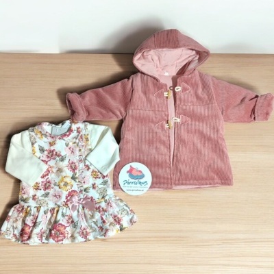 Conjunto de vestido florido e casaco rosa para bebé sobre mesa de madeira.