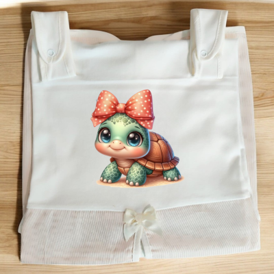 Saco branco com estampa de tartaruga verde de olhos grandes e laço coral, sobre superfície de madeira clara