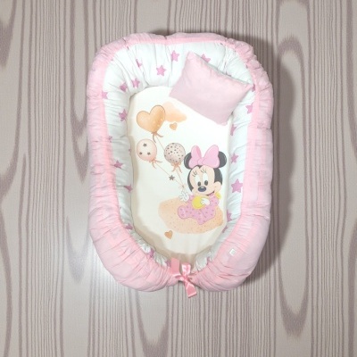 Ninho para bebé branco e rosa com ilustração da Minnie Mouse e balões, sobre chão de madeira clara.