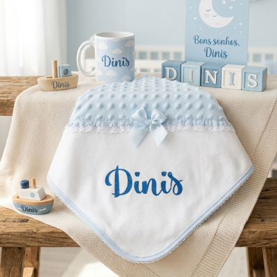 Manta branca com azul, barcos de madeira, caneca, cubos decorativos e placa com texto Bons sonhos, Dinis sobre banco de madeira.