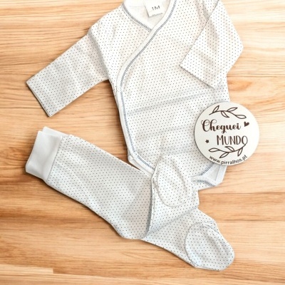 roupa de bebé branca com pontos pretos e placa CHEGUEI MUNDO sobre chão de madeira
