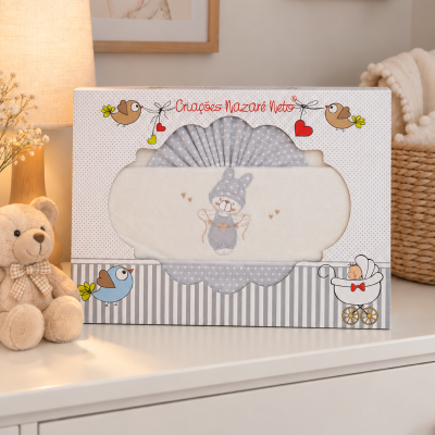 Conjunto de têxteis para bebé cinza e bege numa caixa decorada sobre cómoda branca com peluche e abajur