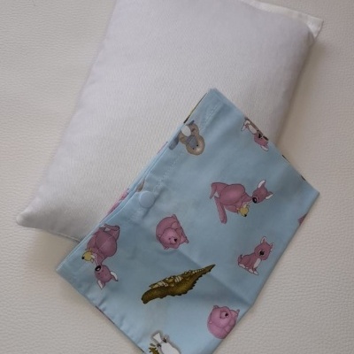 travesseiro branco com capa azul clara estampada com animais cor-de-rosa e outros sobre superfície clara