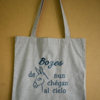 Mala cinzenta de tecido com bordado azul de burro e texto em galego