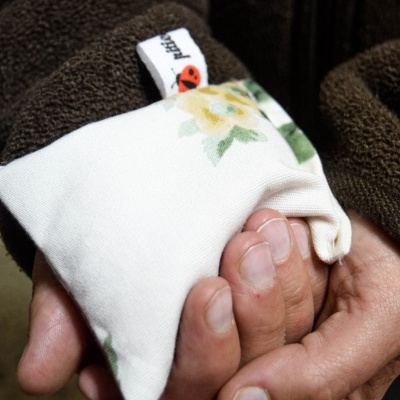 Mãos segurando pequena almofada branca com estampa floral e etiqueta
