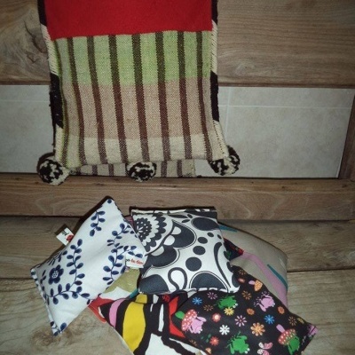 Cinco almofadas pequenas coloridas sobre banco de madeira com manta colorida pendurada