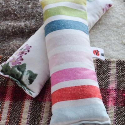 Duas almofadas retangulares coloridas com padrões listrados e florais sobre carpetes de tons neutros.