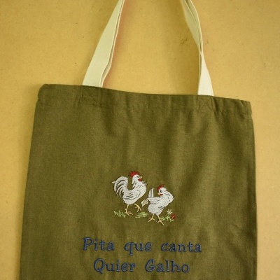 Saco de tecido verde com alças brancas e bordado de galinhas e texto azul