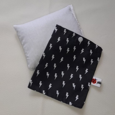 Almofada pequena branca com capa preta de raios brancos e etiqueta visível