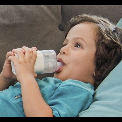 Criança a beber leite de copo de bebé transparente com tampa branca