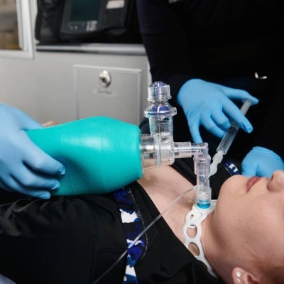 Máscara de ventilação manual azul aplicada a paciente com traqueostomia em ambiente clínico.