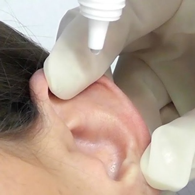 Mão com luva aplicando líquido branco perto da orelha