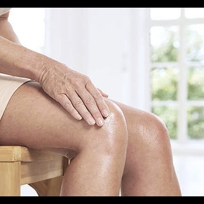 Pessoa a aplicar creme numa perna sentada num banco de madeira