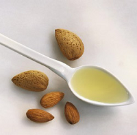 Colher branca com óleo amarelo e amêndoas inteiras e descascadas