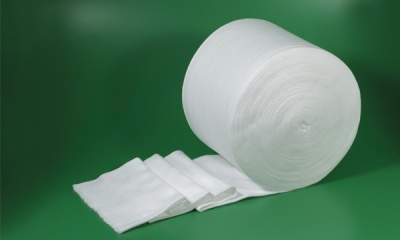 Rolo grosso de tecido branco macio desenrolado em superfície verde