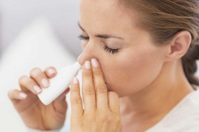 Mulher a aplicar spray nasal branco com tampa azul