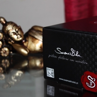 Caixa preta com texto e código QR ao lado de decoração dourada e cortina vermelha