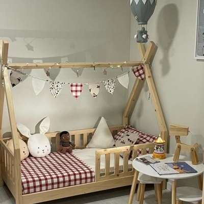 Cama infantil em madeira com roupa de cama xadrez vermelha e branca, mesa pequena com brinquedos e candeeiro de balão cinzento