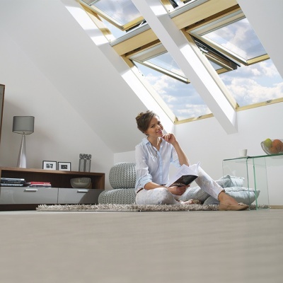 Mulher sentada no chão de uma sala moderna com janelas de telhado abertas e móveis minimalistas.