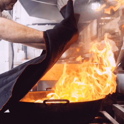 Luva de proteção preta com bordas laranja a ser usada numa cozinha com fogo alto