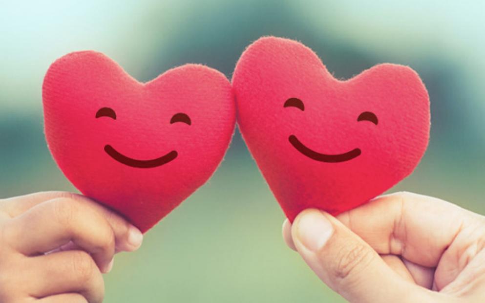 Duas mãos seguram corações vermelhos de espuma com carinhas sorridentes desenhadas