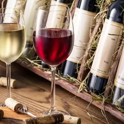 Garrafas de vinho com duas taças, branco e tinto, sobre mesa de madeira