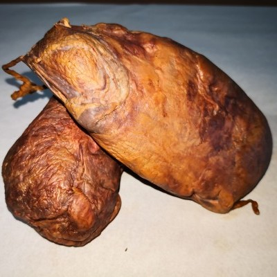 Dois enchidos fumados castanhos com textura enrugada sobre superfície branca