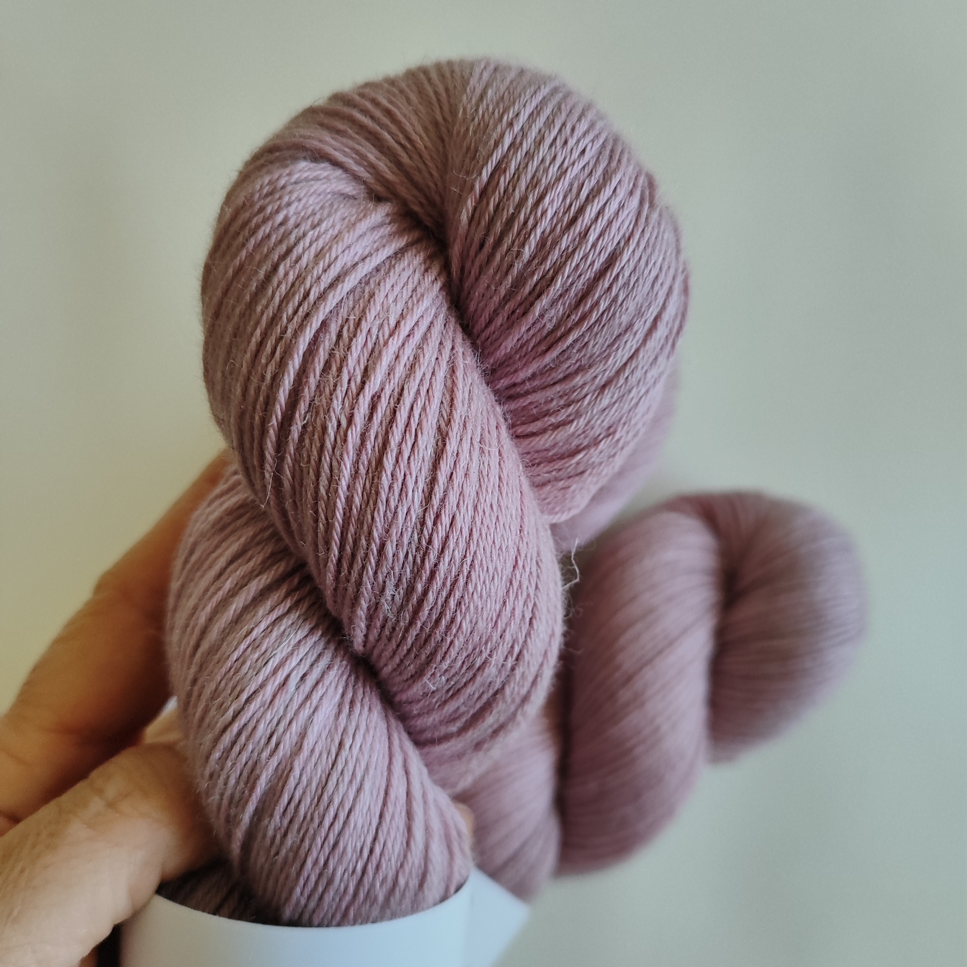 LINEN SILK Novelo de lã cor de rosa claro com etiqueta branca e mão a segurá-lo
