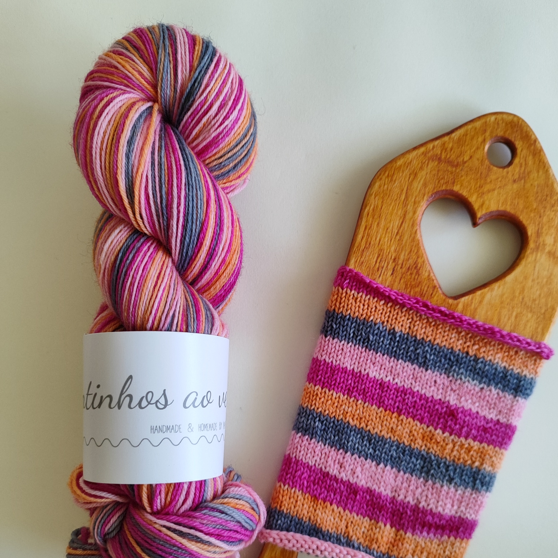 Self Striping SOCK Lã multicolorida enrolada ao lado de peça de madeira com recorte de coração e malha às riscas