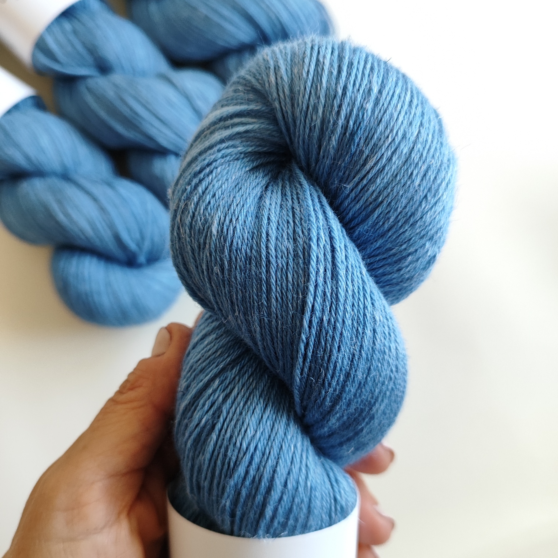 LINEN SILK Novelo de lã azul claro segurado pela mão sobre fundo branco
