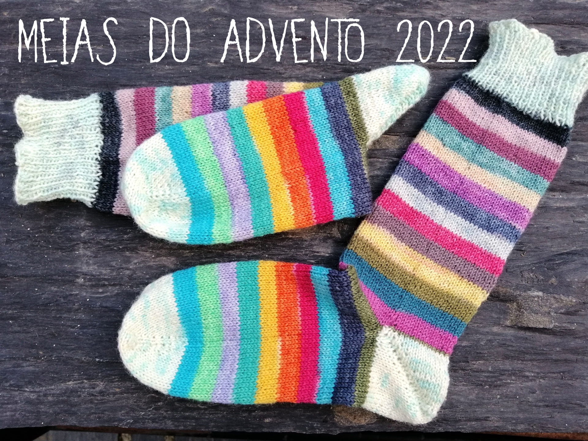 MEIAS DO ADVENTO Três meias coloridas com riscas sobre madeira com texto 'MEIAS DO ADVENTO 2022'