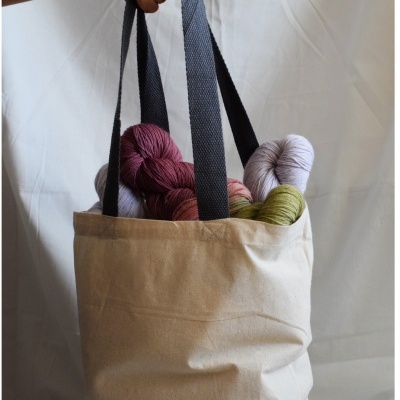 Saco de tecido bege com alças pretas e novelos de lã coloridos no interior