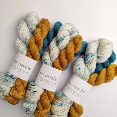 Conjuntos de novelos de lã branco com manchas azuis, azul e amarelo mostarda com etiquetas 'ao vento'