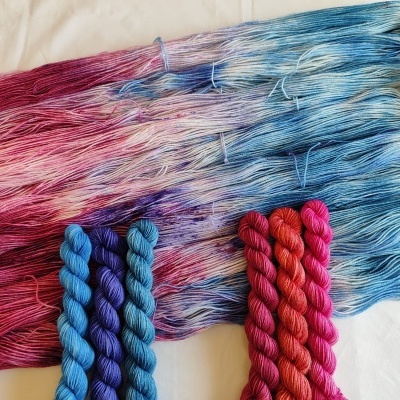 Fios de lã tingidos em degradê azul, rosa e vermelho com novelos coloridos sobre tecido branco