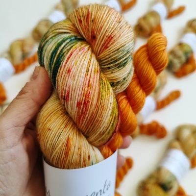 Novelo colorido de fio de lã com etiquetas brancas e novelos laranja ao fundo