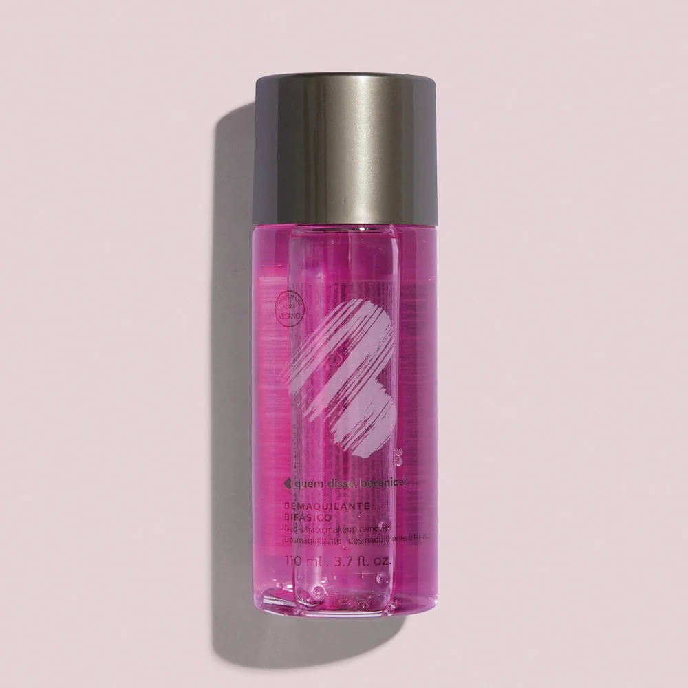 Desmaquilhante Bifásico 110ml Frasco transparente com líquido rosa e tampa prateada sobre fundo rosa claro.