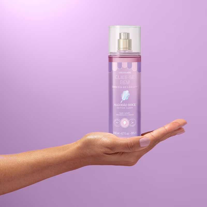 Body Splash Cuide-se Bem Doces Delírios Algodão Doce 200 ml Frasco de spray corporal lilás com texto branco e tampa transparente em mão de pele morena sobre fundo lilás