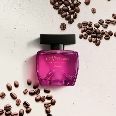 Perfume rosa com tampa preta rodeado por grãos de café