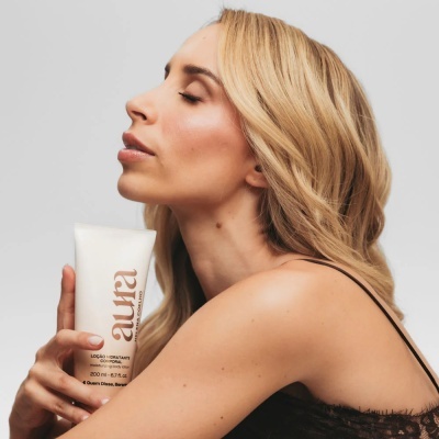 Frasco branco de creme hidratante Aura com mulher loira segurando o frasco