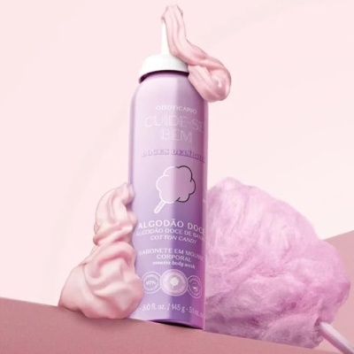 Frasco lilás de mousse corporal com algodão doce rosa e fundo rosa claro