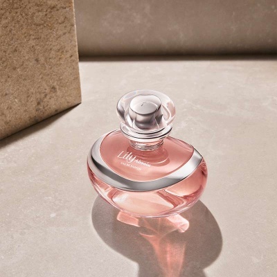 Frasco de perfume rosa com tampa transparente sobre superfície bege texturada