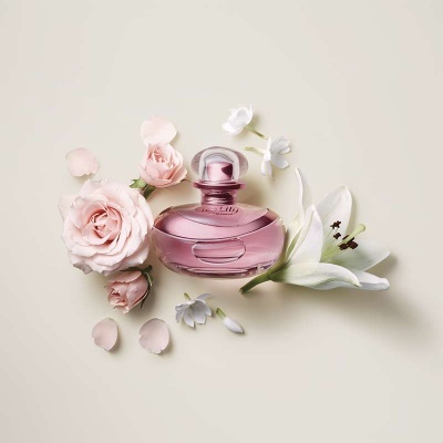 Frasco de perfume rosa com flores ao redor