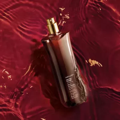 Frasco de spray corporal marrom escuro com tampa dourada sobre líquido vermelho