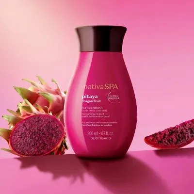 Frasco rosa de óleo corporal Nativa SPA Pitaya junto a pitayas cortadas em fundo rosa