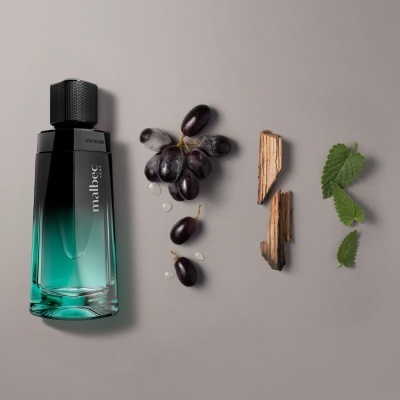 Frasco de perfume Malbec ao lado de uvas pretas, madeira e folhas verdes