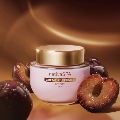Frasco creme perfumado nativaSPA ameixa com tampa dourada ao lado de ameixas frescas