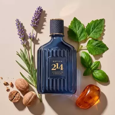 Frasco azul escuro com tampa preta e texto dourado rodeado por plantas e frutos sobre fundo bege