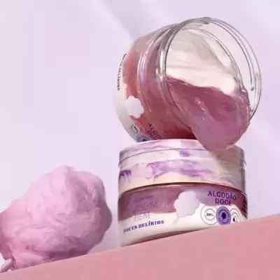 Creme corporal lilás em frasco transparente com algodão doce rosa ao lado
