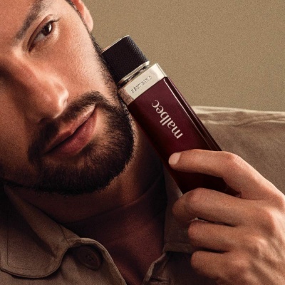 Homem segurando frasco de perfume vinho com tampa preta e detalhes prateados