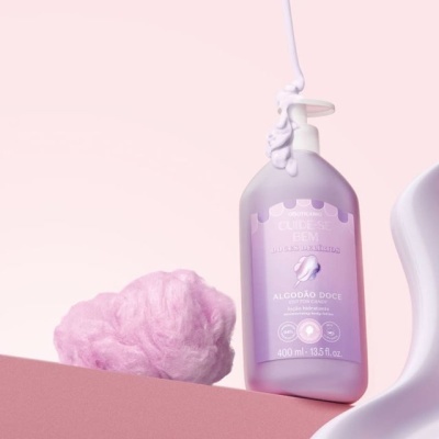 Frasco lilás com loção hidratante algodão doce ao lado de algodão doce rosa em fundo rosa